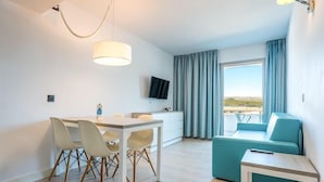 A modern hotel room with a dining table, chairs, a sofa, a TV, and a balcony with curtains. - Aparthotel THB Guya Playa (Capdepera)