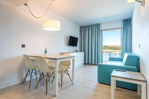 Une chambre d’hôtel moderne équipée d’une table à manger, de chaises, d’un canapé, d’une télévision et d’un balcon avec des rideaux.