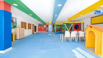 Un área de juegos interior, llena de color, con piso azul, una estructura de juego y una casita amarilla.
