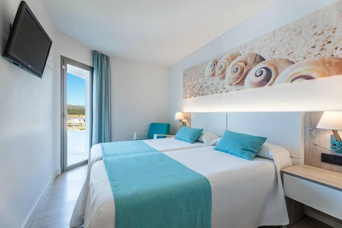 A hotel room with a bed, a chair, a TV, and a painting of fish on the wall.