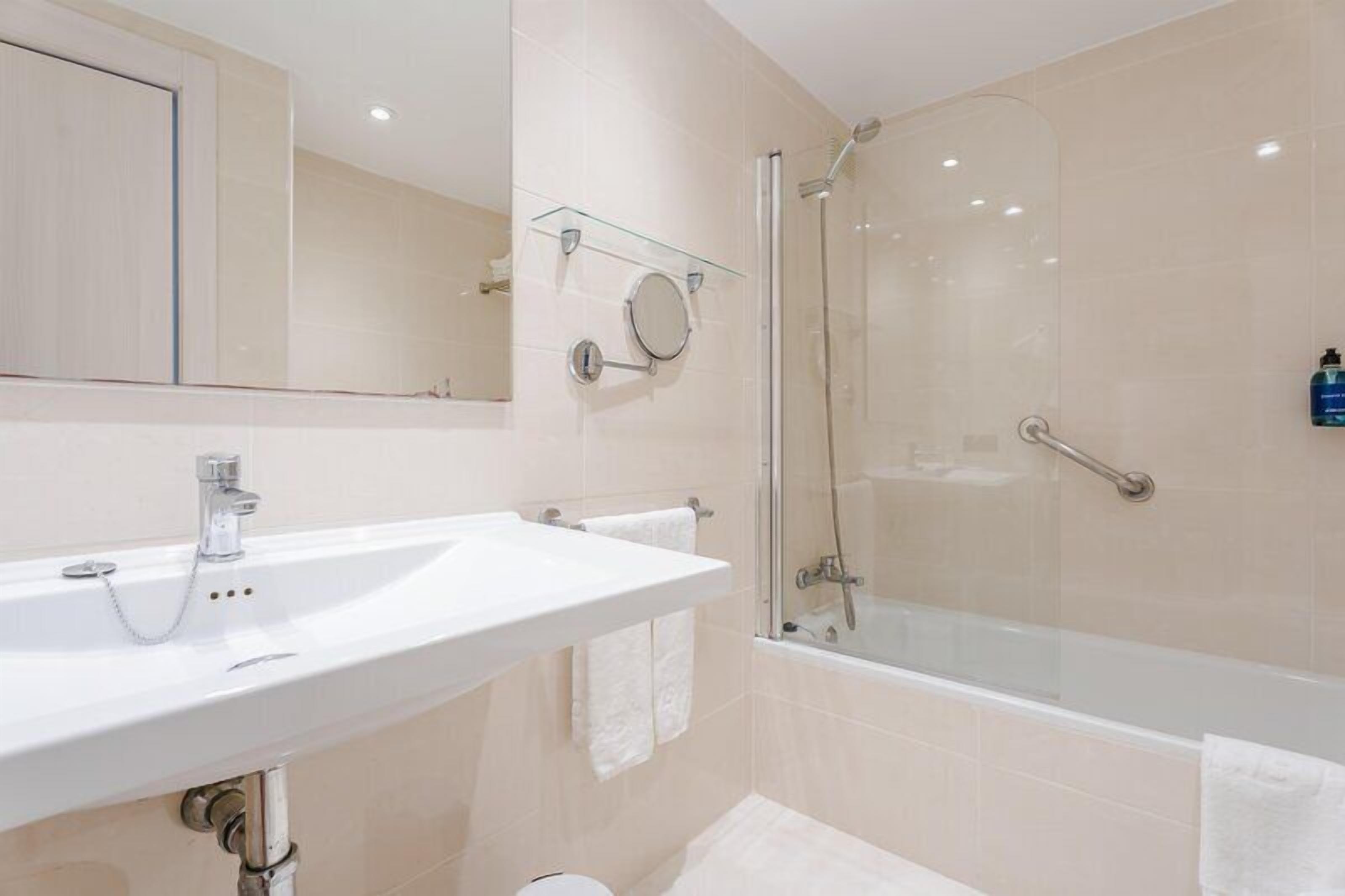 A modern bathroom with a white sink, mirror, and glass-enclosed shower.
