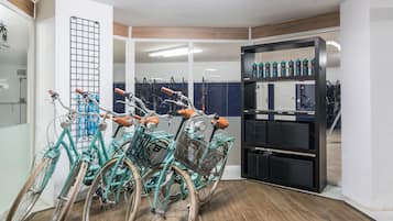 Una habitación con bicicletas estacionadas contra la pared, un soporte con cascos y un estante con botellas de agua.