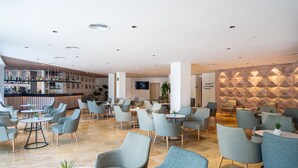 Ein moderner Lounge-Bereich mit verschiedenen Sitzgelegenheiten, einer Bar im Hintergrund und einer Wand mit geometrischem Muster.