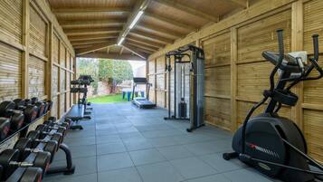 Een overdekte fitnessruimte met trainingsapparatuur, waaronder gewichten, een bank, een loopband en een hometrainer.