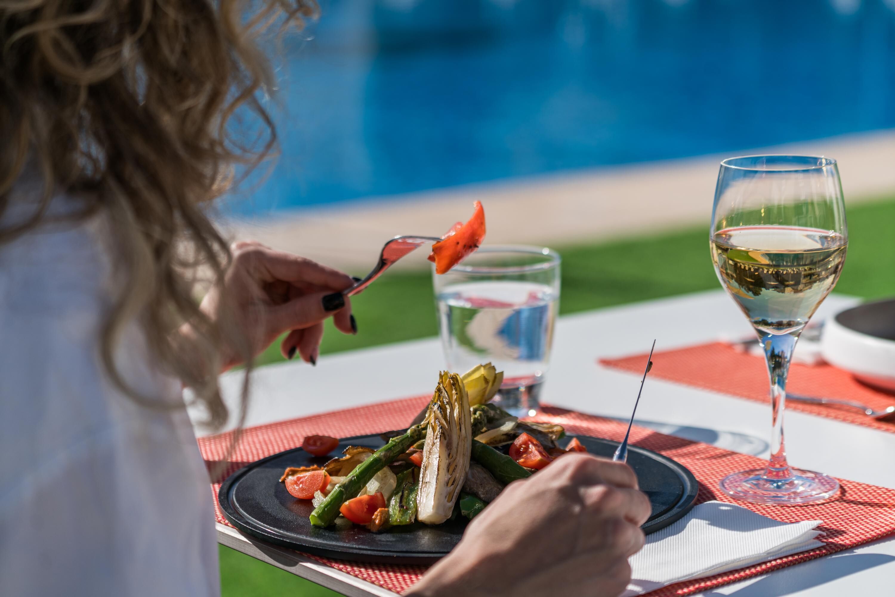 Une table à manger avec une assiette de nourriture, un verre de vin blanc et un verre d’eau.