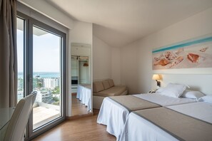 Habitación de hotel con un ventanal grande, un sofá, dos camas y un cuadro de conchas marinas.