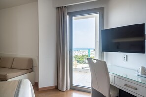 Une chambre d’hôtel moderne, dotée d’un canapé, d’un bureau avec un téléviseur à écran plat et d’une grande fenêtre donnant sur la ville.