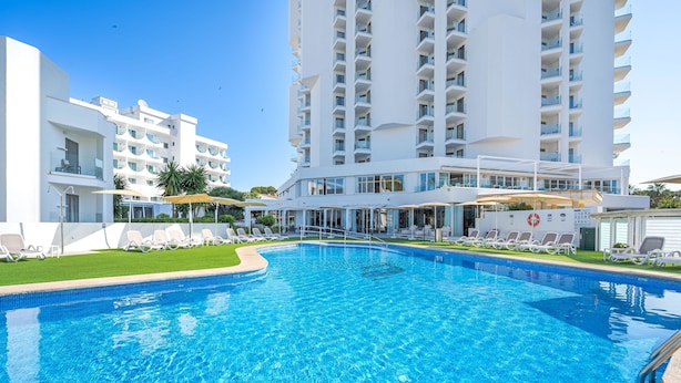 Une piscine avec des chaises longues et, au fond, un bâtiment doté de balcons.
