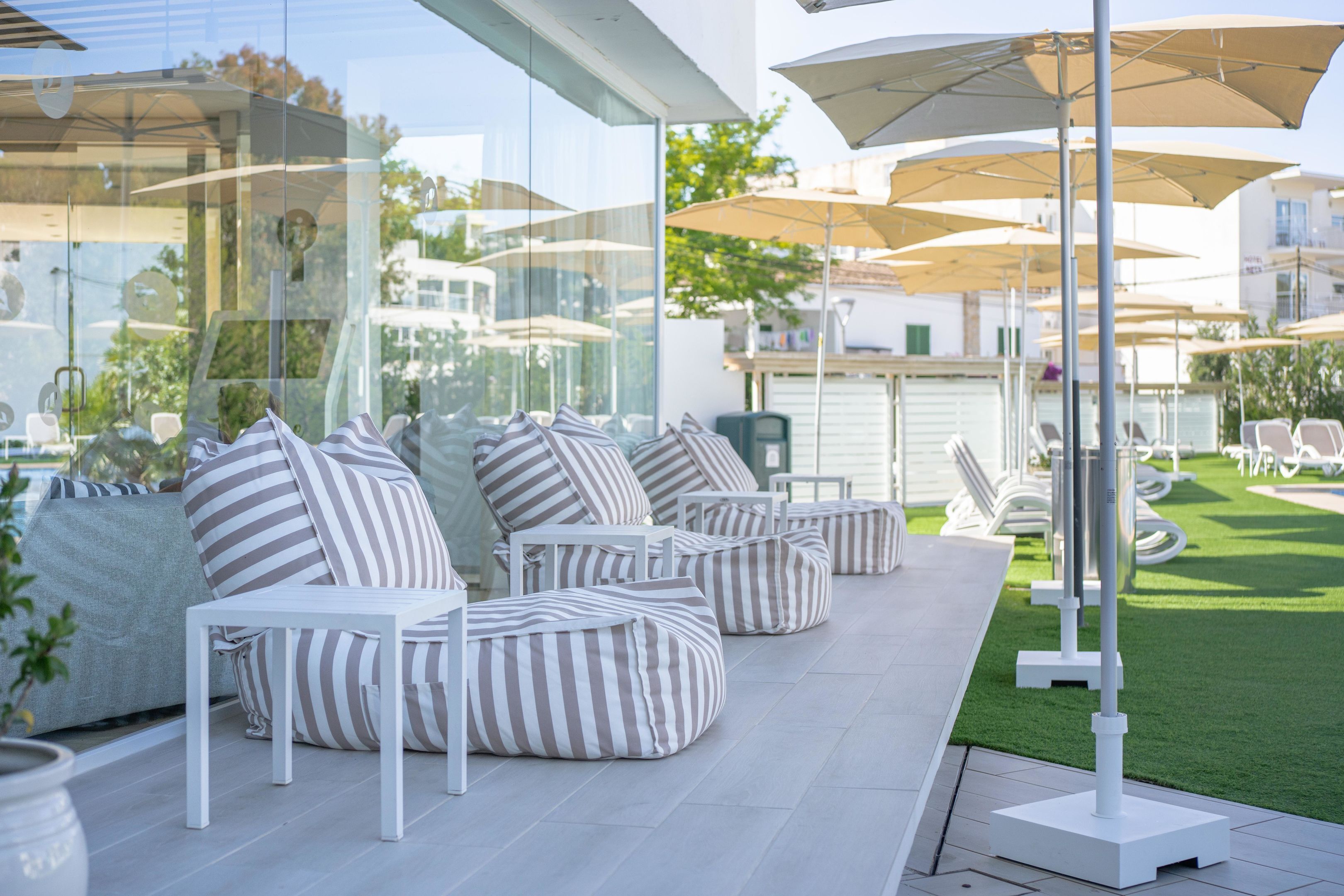 A modern outdoor seating area with striped cushions and white furniture, surrounded by umbrellas and a well-maintained lawn.