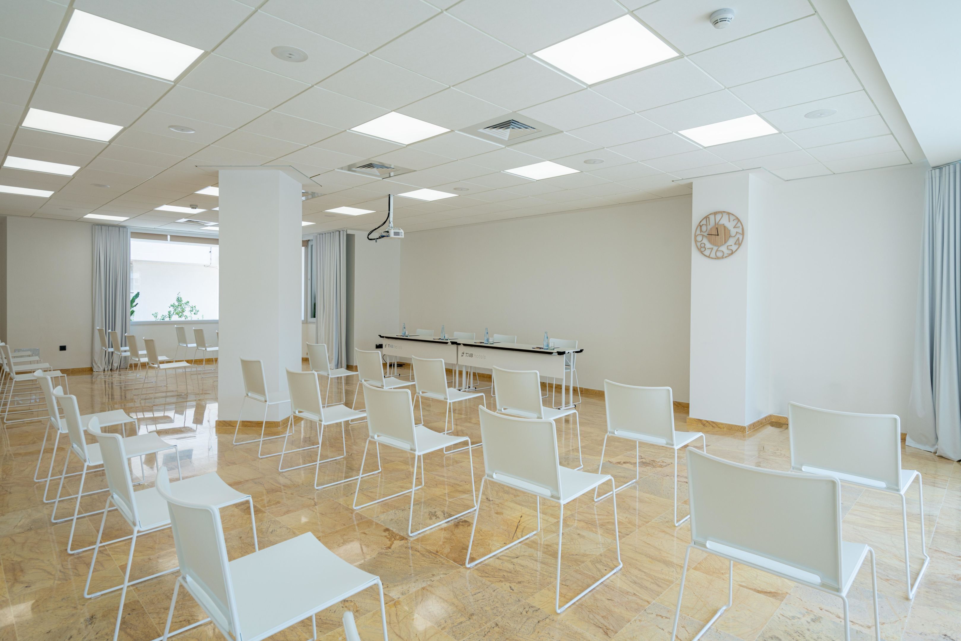 Een vergaderruimte met witte stoelen en tafels, een projecter en een klok aan de muur.