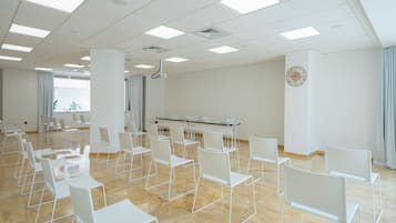 Een vergaderruimte met witte stoelen en tafels, een projecter en een klok aan de muur.