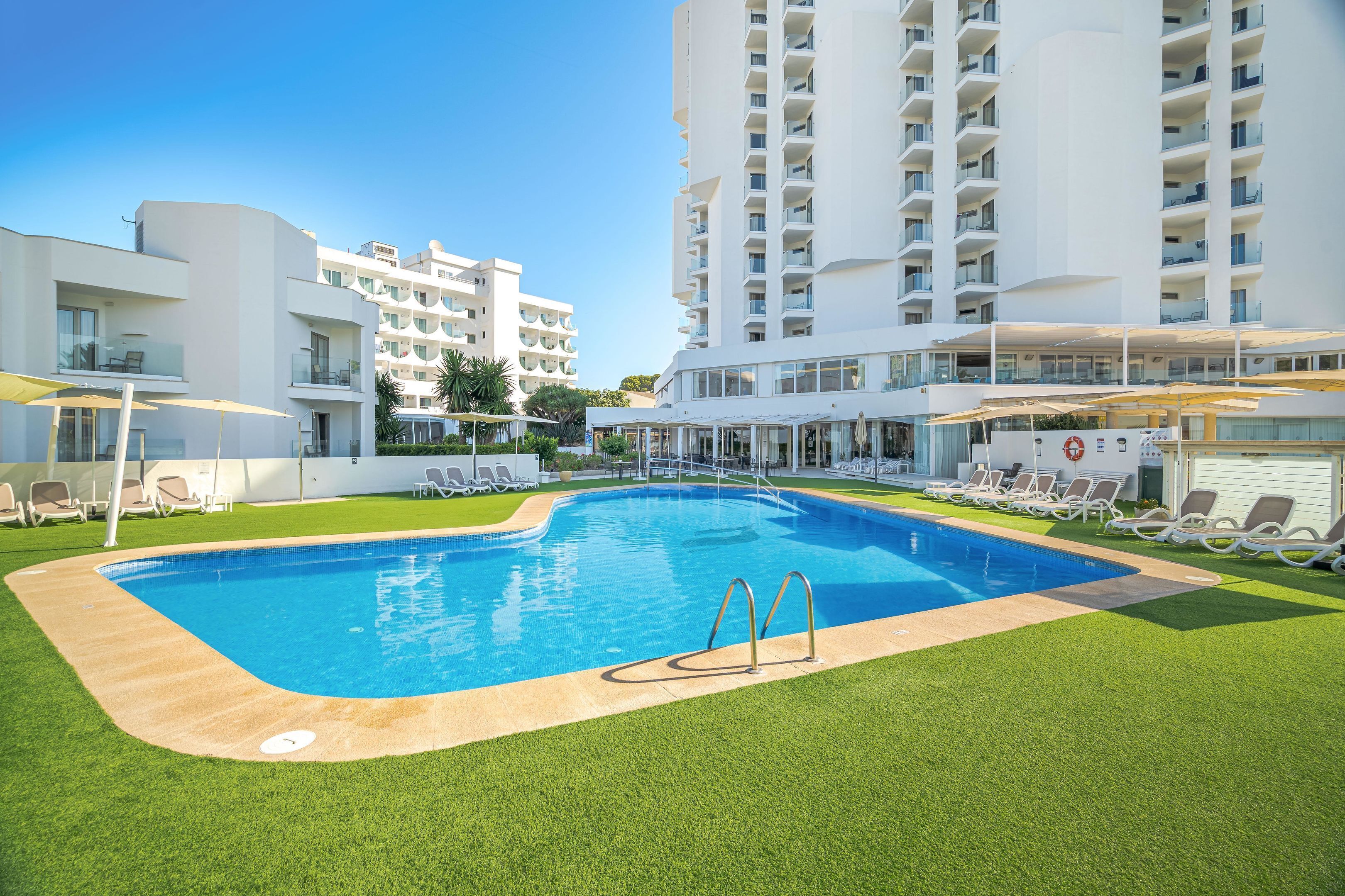 A swimming pool with a surrounding grassy area, lounge chairs, and a modern building with balconies.