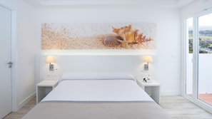 A modern hotel room with a large bed, two bedside tables with lamps, a wall-mounted artwork, and a view through a large window.