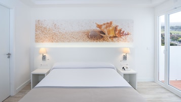 Una habitación de hotel moderna con una cama grande, dos mesitas de noche con lámparas, una obra de arte en la pared y vistas a través de un amplio ventanal.