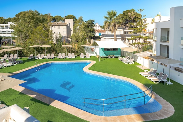 Una piscina con tumbonas y un carrito de aperitivos.
