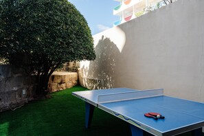 Een tafeltennistafel met net in een buitengebied met kunstgras en een boom.