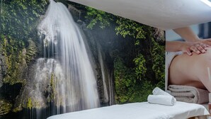 Un espace spa comprenant une table de massage, une fresque représentant une cascade et une vue sur une forêt luxuriante.