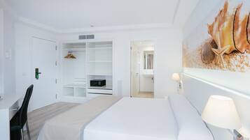 Habitación de hotel con cama, escritorio, silla, armario y baño visible a través de una puerta abierta.