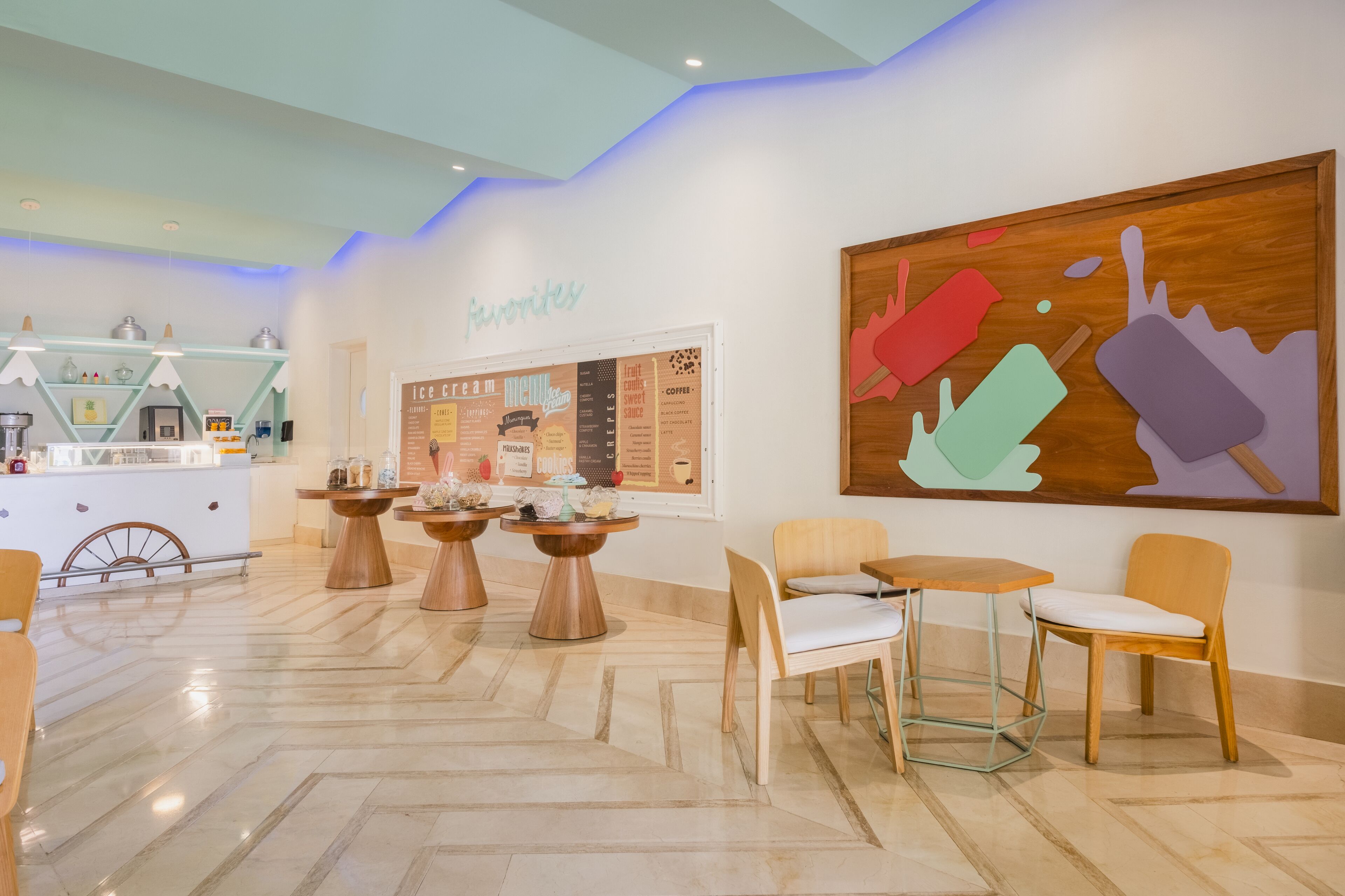 A café area with wooden tables and chairs, a menu board, and a wall with a colorful ice cream design.