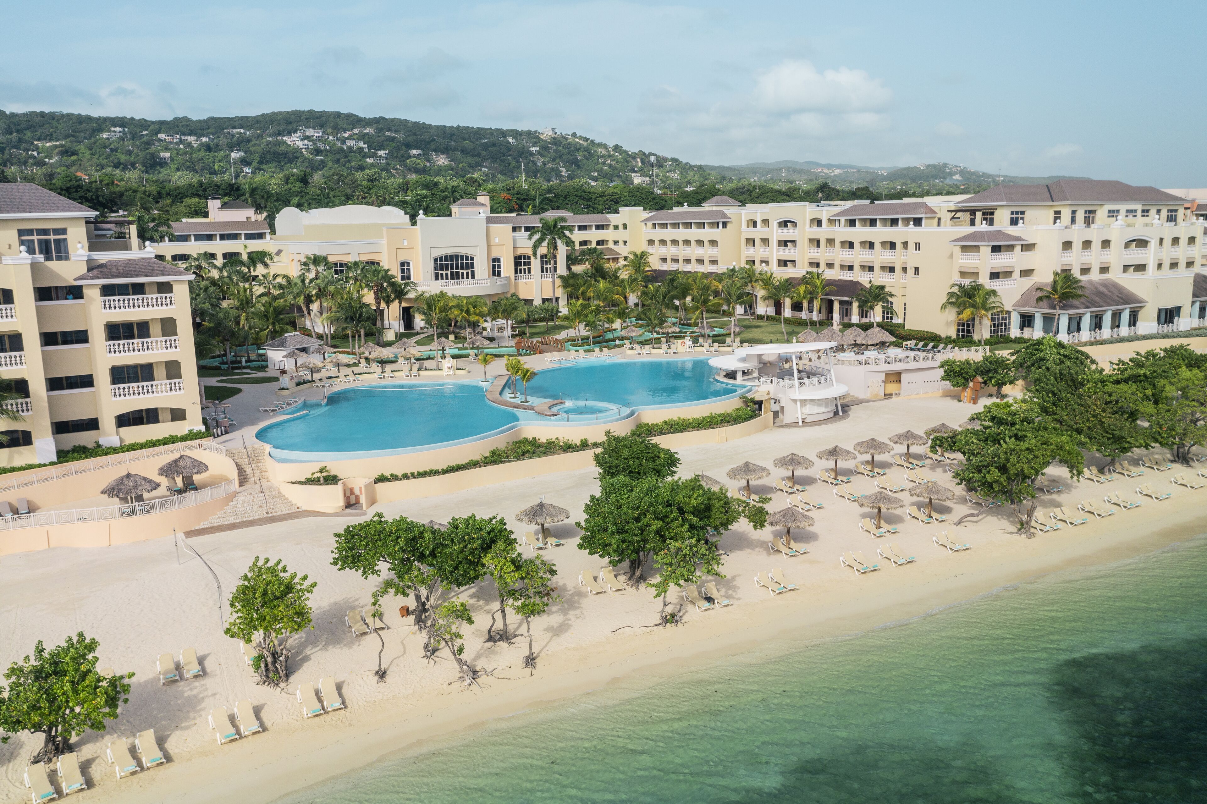A resort with multiple swimming pools, a beach, and a mountainous backdrop.