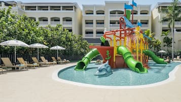 Relax by the pool with lounge chairs and umbrellas, surrounded by a children's water play area with slides and a dolphin figure.