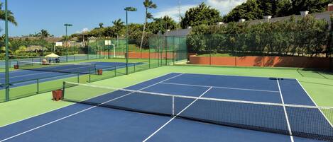 A tennis court with a net, surrounded by a fence and palm trees.