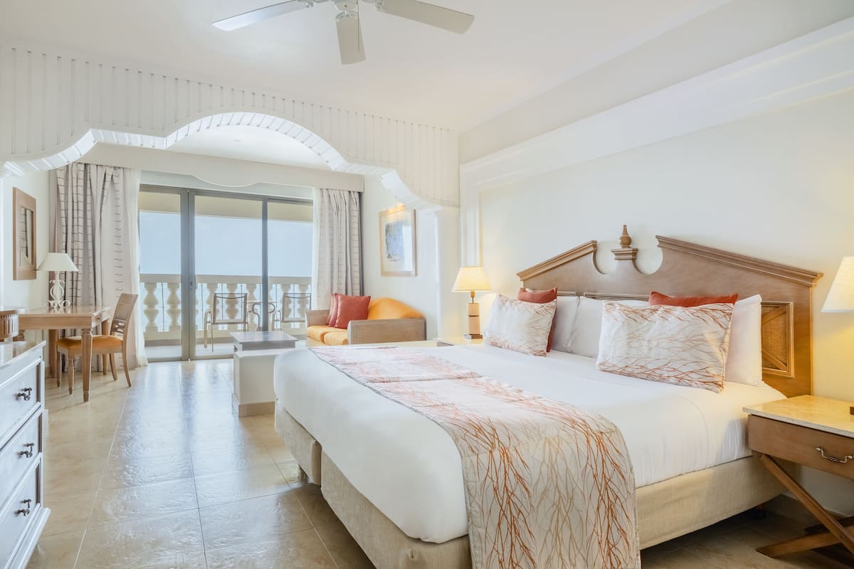 A hotel room with a large bed, a desk, and a balcony with curtains.