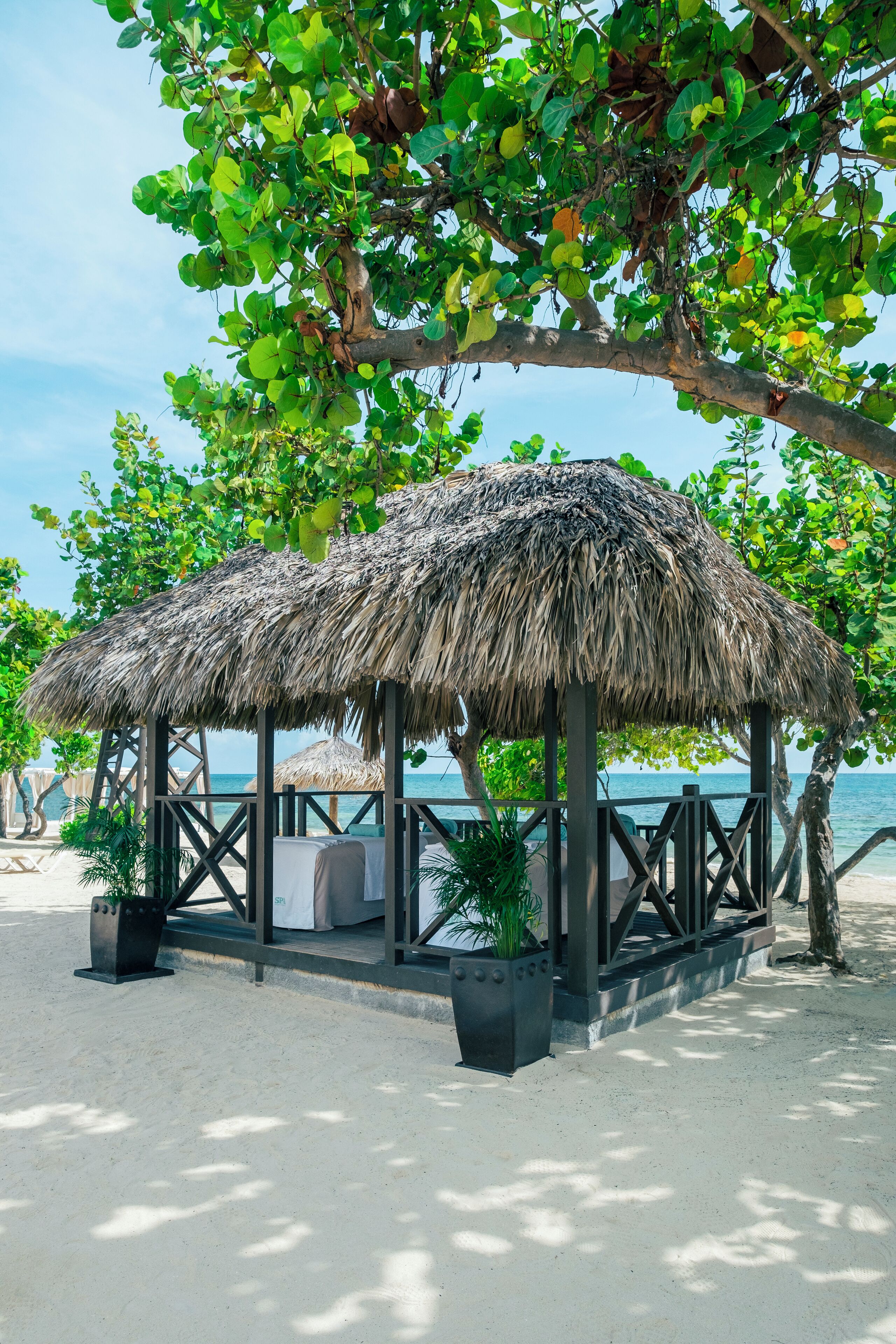 A beachside structure with a thatched roof, surrounded by sand and greenery.