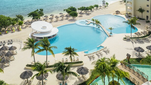 A resort with a large central pool, smaller pools, and a beach area with umbrellas and lounge chairs. - Iberostar Waves Rose Hall Beach - All Inclusive (Montego Bay)