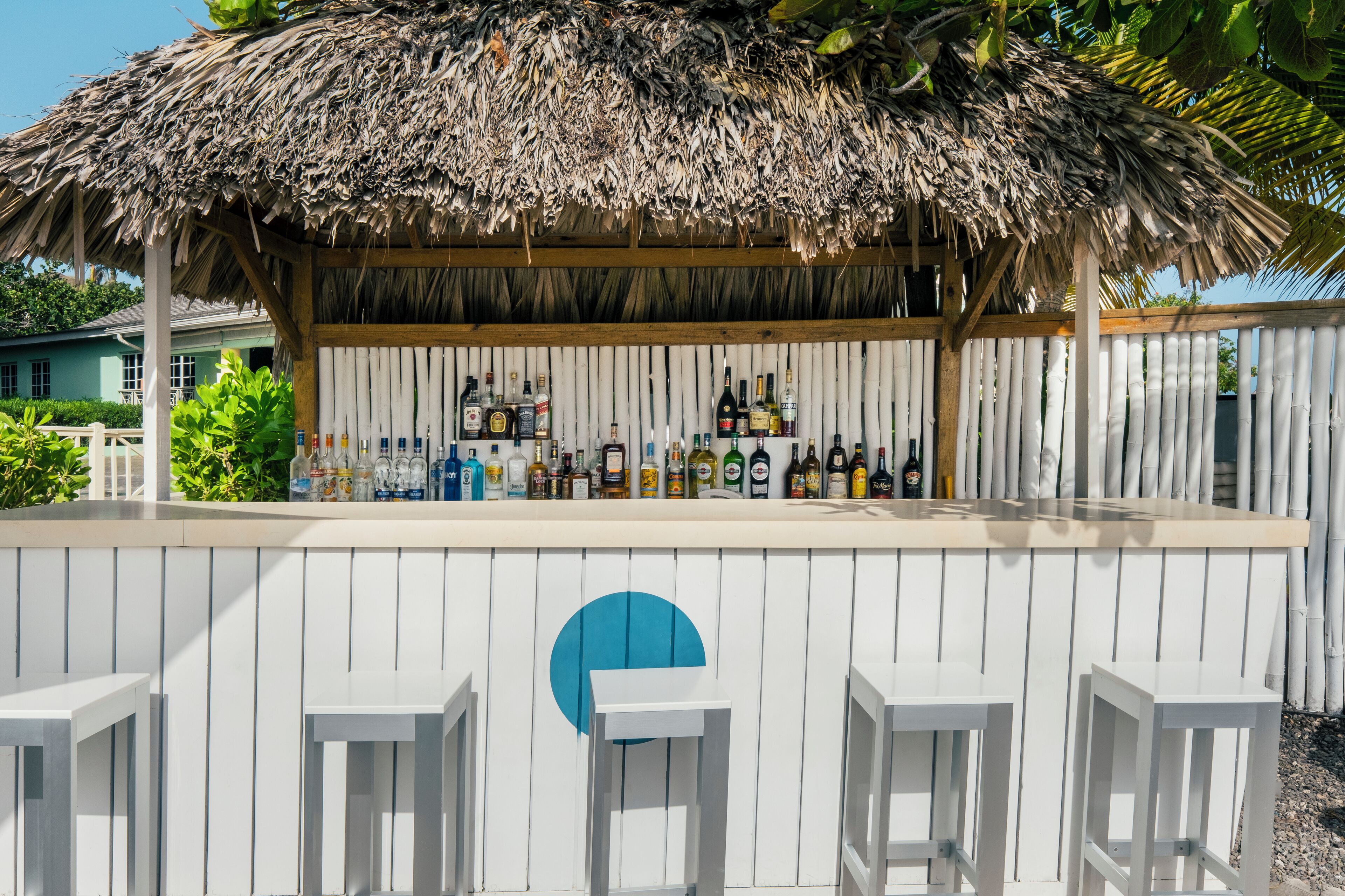 Una zona de bar con techo de paja, paneles de madera blanca y una variedad de botellas.