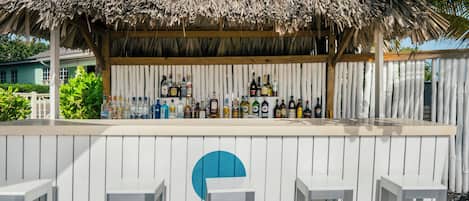Una zona de bar con techo de paja, paneles de madera blanca y una variedad de botellas.