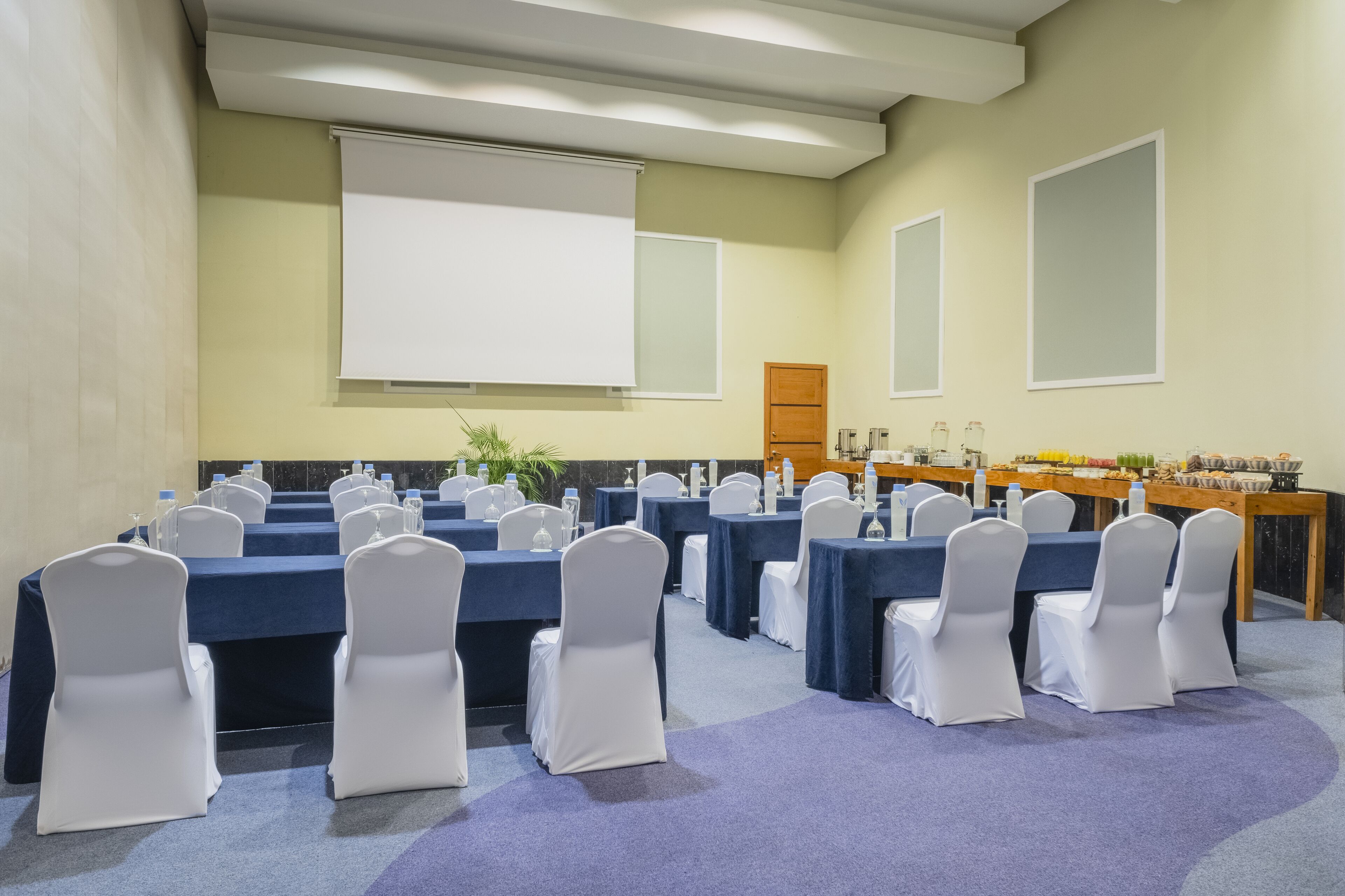 Ein Konferenzraum mit Tischen und Stühlen, einer Projektionsleinwand und einem Buffet.