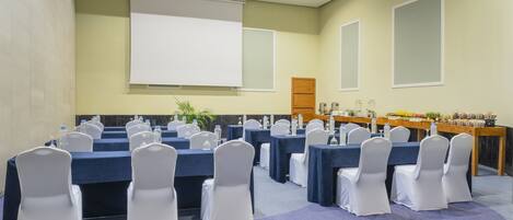 Ein Konferenzraum mit Tischen und Stühlen, einer Projektionsleinwand und einem Buffet.