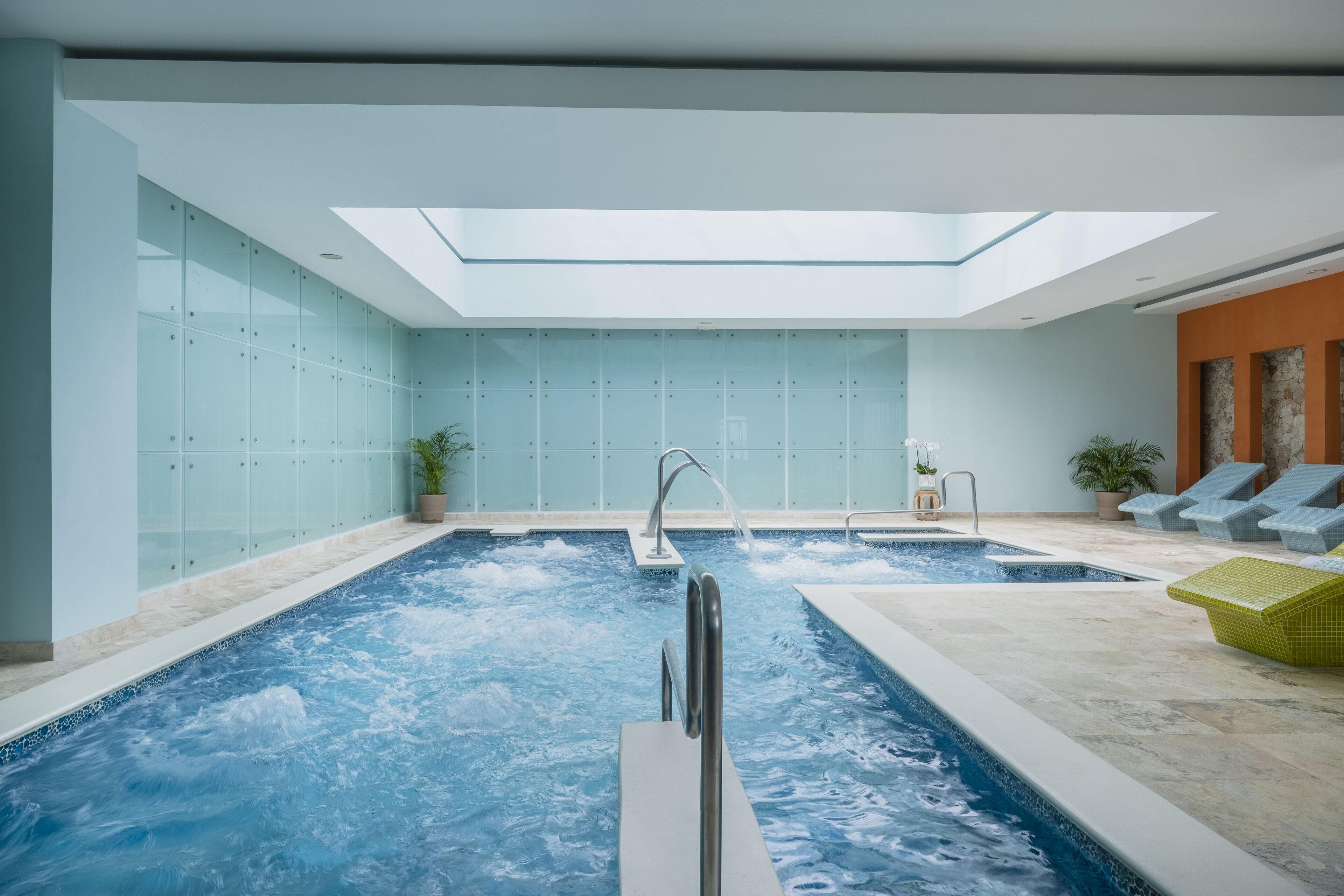 Ein Hallenbad mit Oberlichter, Liegestühlen und einer Steinwand.