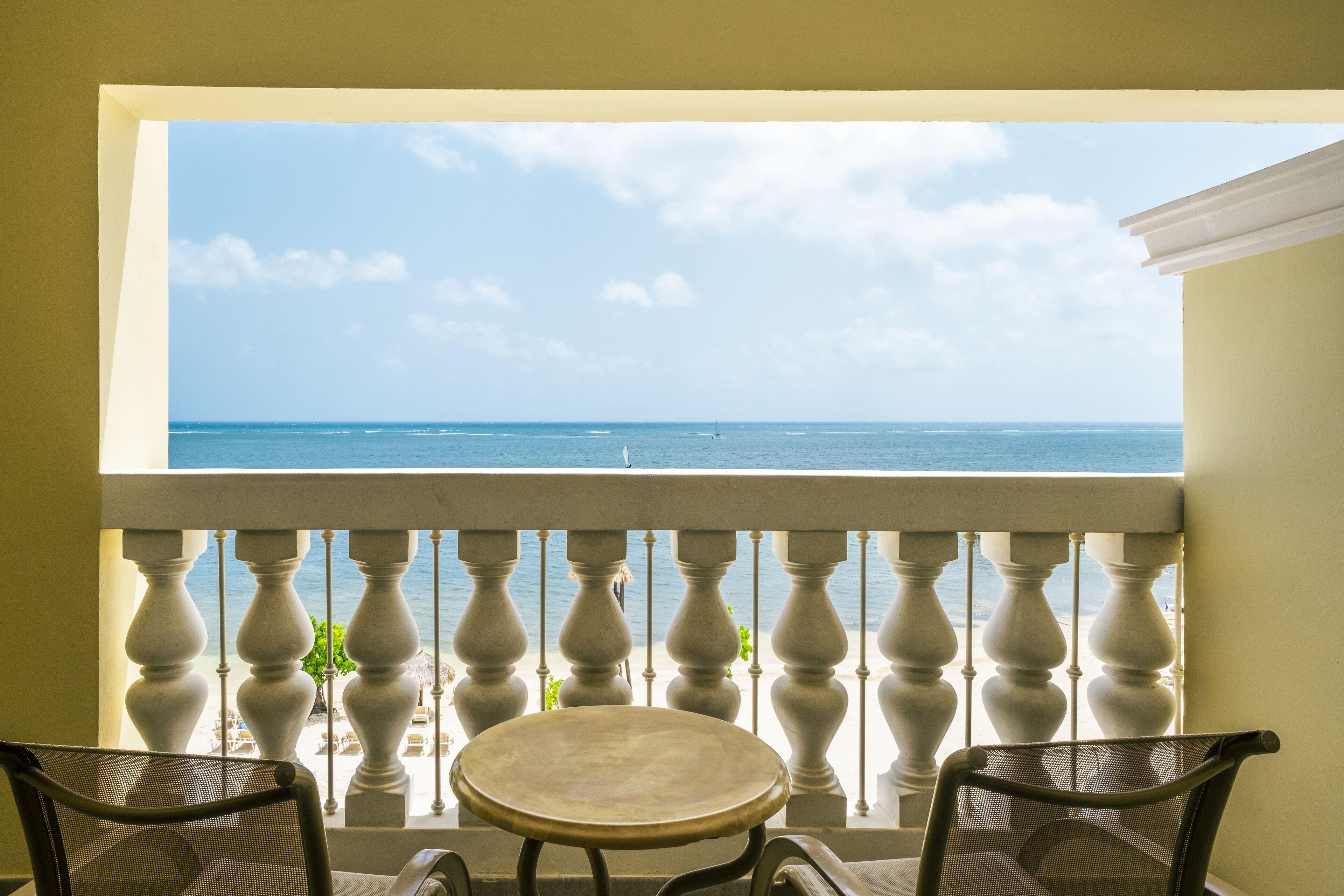 A balcony with a view of the ocean, a round table, and two chairs.