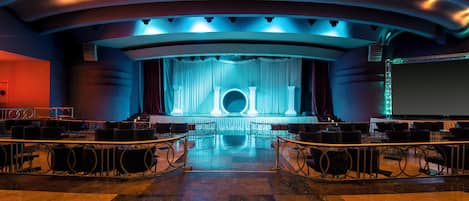A theater with tiered seating, a stage with curtains, and a large screen.