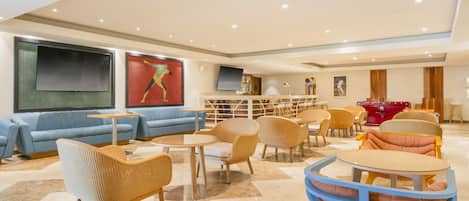 A modern lobby with seating areas, a TV mounted on the wall, and artwork.