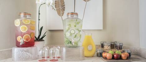 A kitchen counter with two glass jars containing citrus slices, a potted orchid, and a variety of fruits and jars.