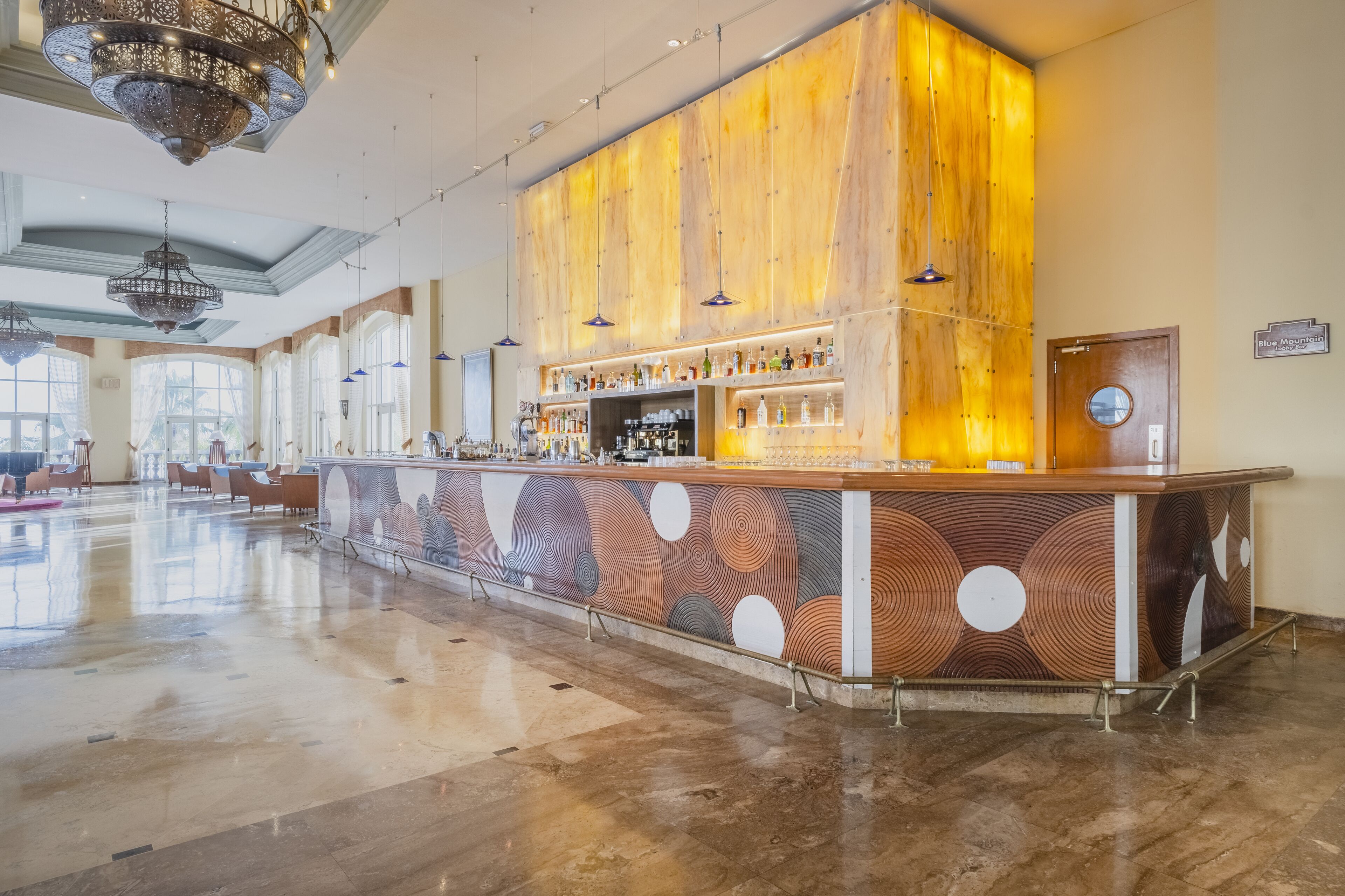 A spacious lobby with a central bar area featuring a wooden panel design and a variety of bottles.