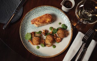 Un plato con comida, una copa de vino y cubiertos sobre una mesa.