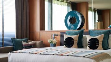 Una habitación de hotel con una cama grande, un adorno azul redondo en la pared y una ventana con persianas.