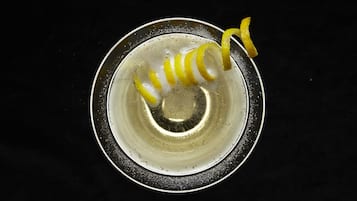 Una ciotola metallica con una spirale di scorza di limone su sfondo scuro.