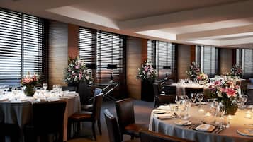 Un restaurante con varias mesas dispuestas para comer, con paneles de madera oscura y amplias ventanas con persianas.