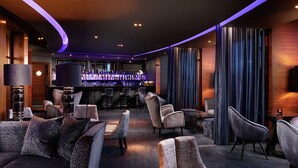 Un espace lounge moderne avec des canapés et des fauteuils, un bar proposant une grande variété de boissons, et un plafond incurvé doté d’un éclairage d’ambiance.