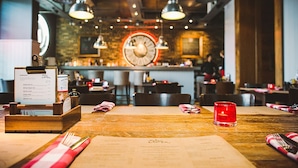A restaurant interior with wooden tables, hanging pendant lights, and a menu stand. - Aviator Hampshire (Farnborough)