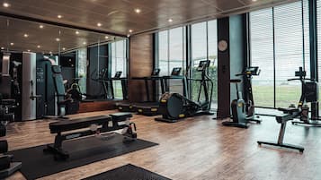 Un gimnasio moderno con diversos equipos de ejercicio, ventanas amplias y suelo de madera.