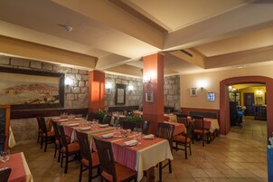 Un restaurante con varias mesas y sillas, paredes de piedra y un mural a la izquierda.