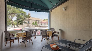 A covered outdoor seating area with wicker chairs and tables, a lounge area with metal chairs, and a view of a building with a dome.