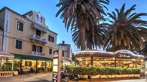 A restaurant with outdoor seating, a motorcycle parked in front, and a palm tree in the background. - Villa Pattiera (Konavle)