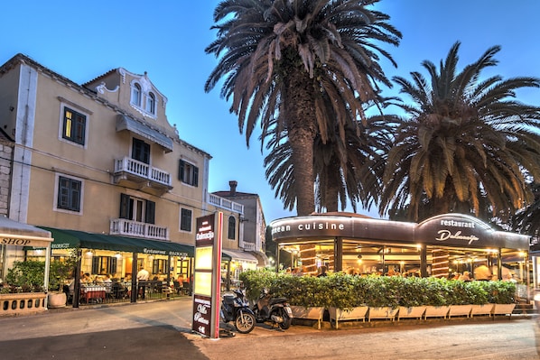 Un restaurante con terraza, una motocicleta estacionada al frente y una palmera al fondo.